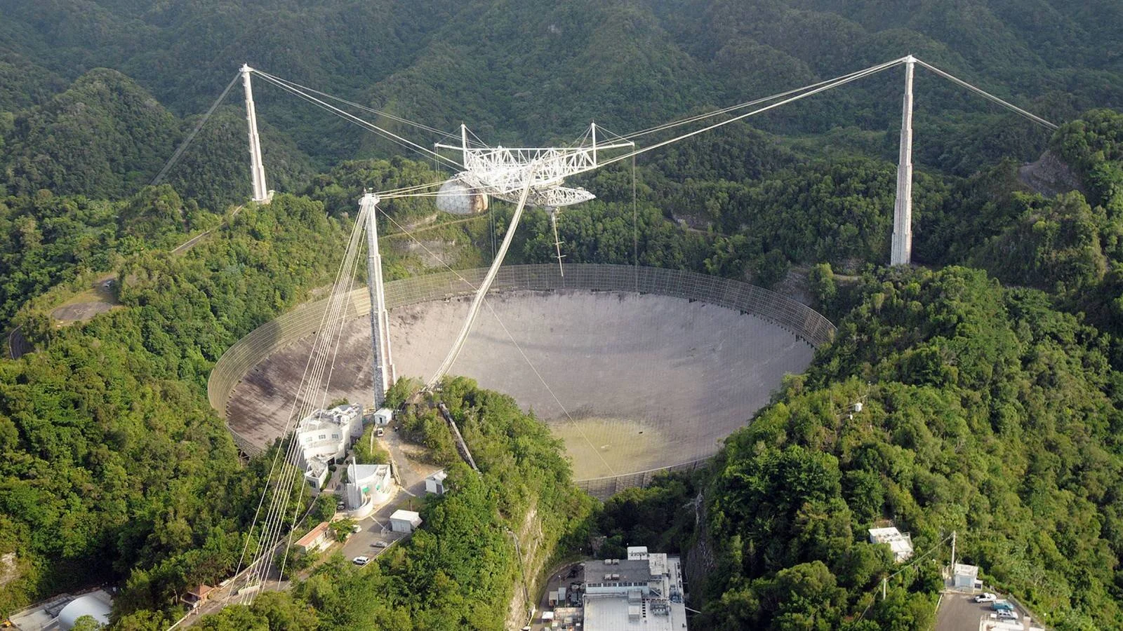 Vista aérea del enorme disco reflector del Observatorio de Arecibo rodeado de montañas boscosas en Puerto Rico.