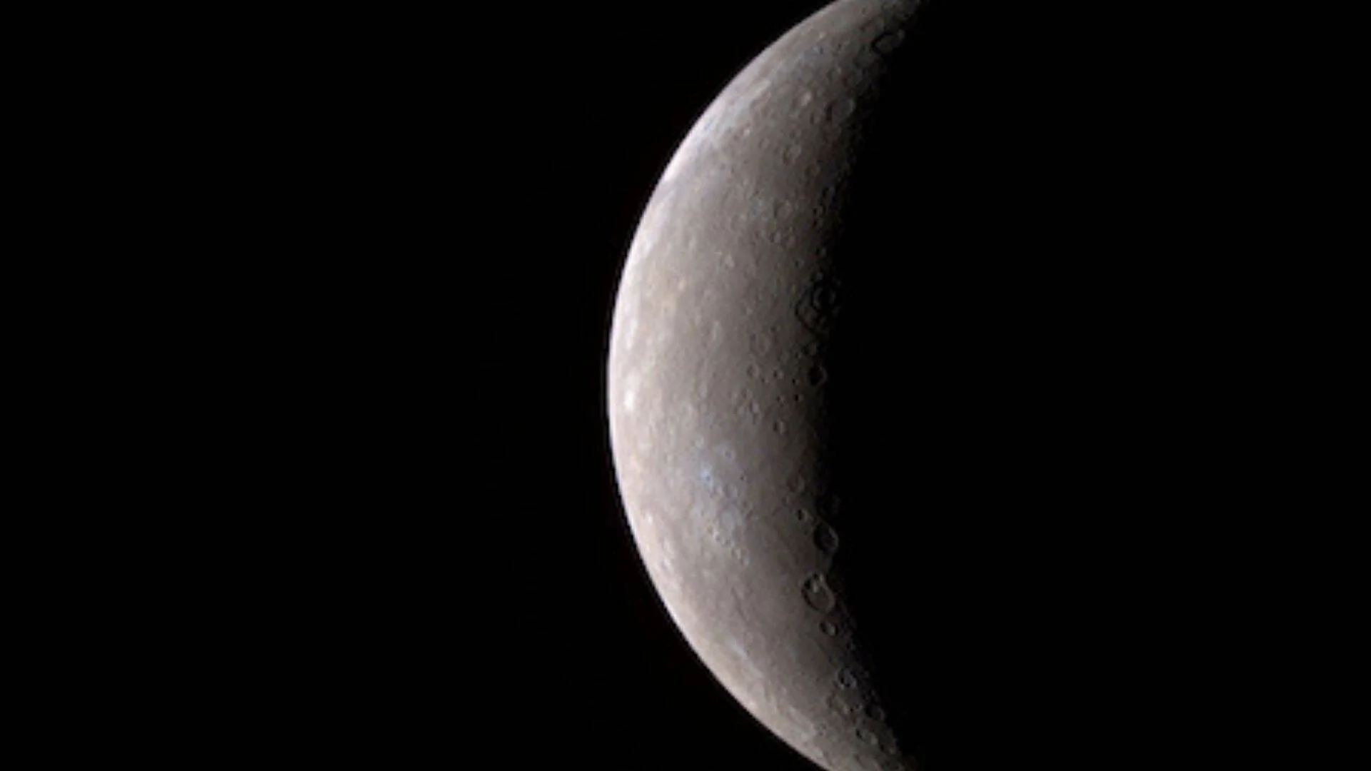 Vista parcial de Mercurio con su superficie gris cubierta de cráteres sobre fondo negro del espacio.