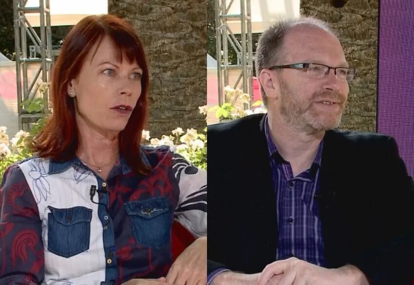 Una mujer de cabello pelirrojo y un hombre con gafas participan en una entrevista televisiva al aire libre.