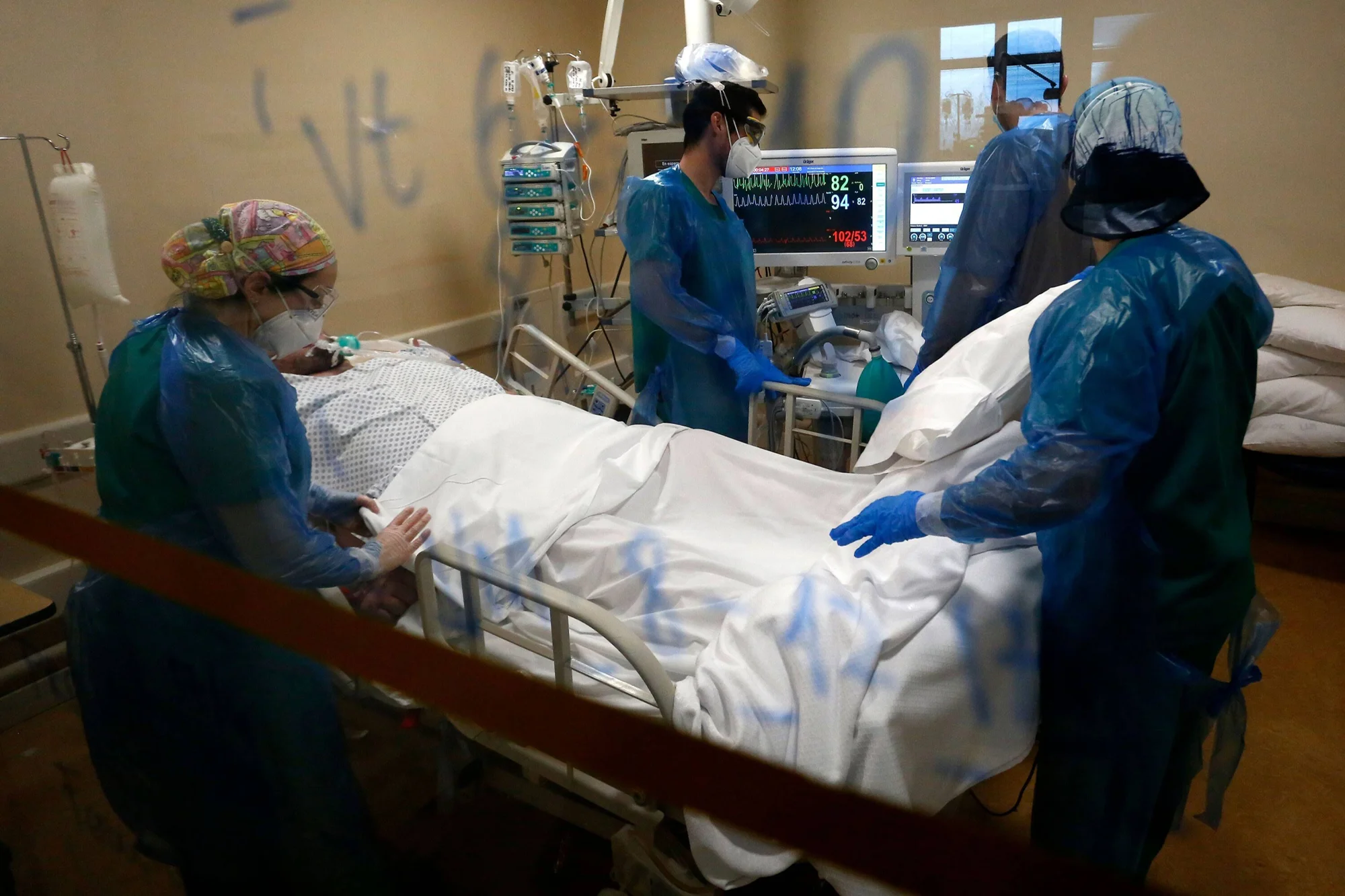 Tres profesionales de la salud con equipo de protección atienden a un paciente en cama de terapia intensiva rodeado de monitores.