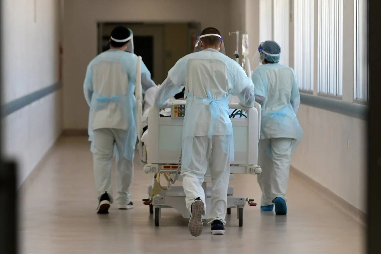 Tres profesionales de salud con equipo de protección trasladan una camilla con paciente por un pasillo hospitalario.