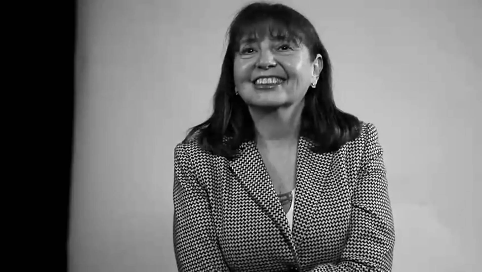 Mujer de mediana edad con saco estampado sonríe ampliamente en una fotografía en blanco y negro.