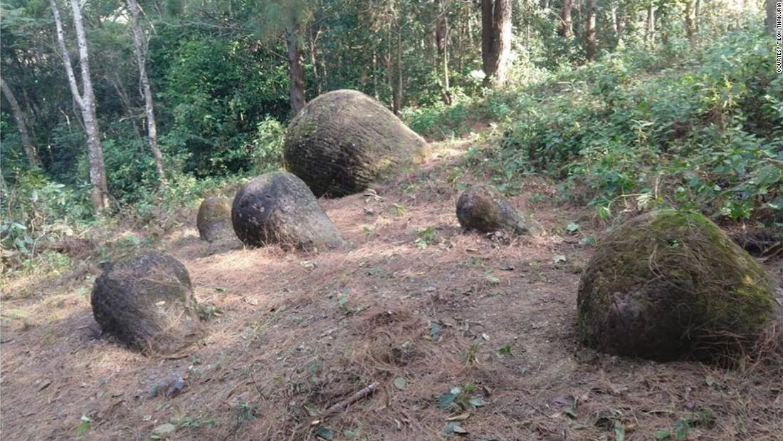 Grupo de grandes rocas esféricas de piedra dispersas en un claro de bosque, cubiertas parcialmente de musgo.