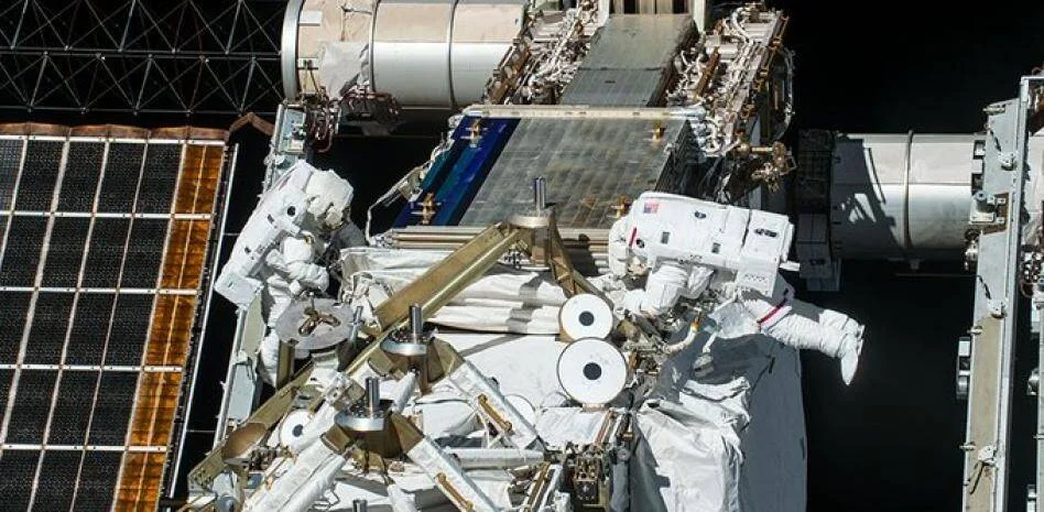 Dos astronautas con trajes espaciales realizan una caminata espacial en el exterior de la Estación Espacial Internacional.