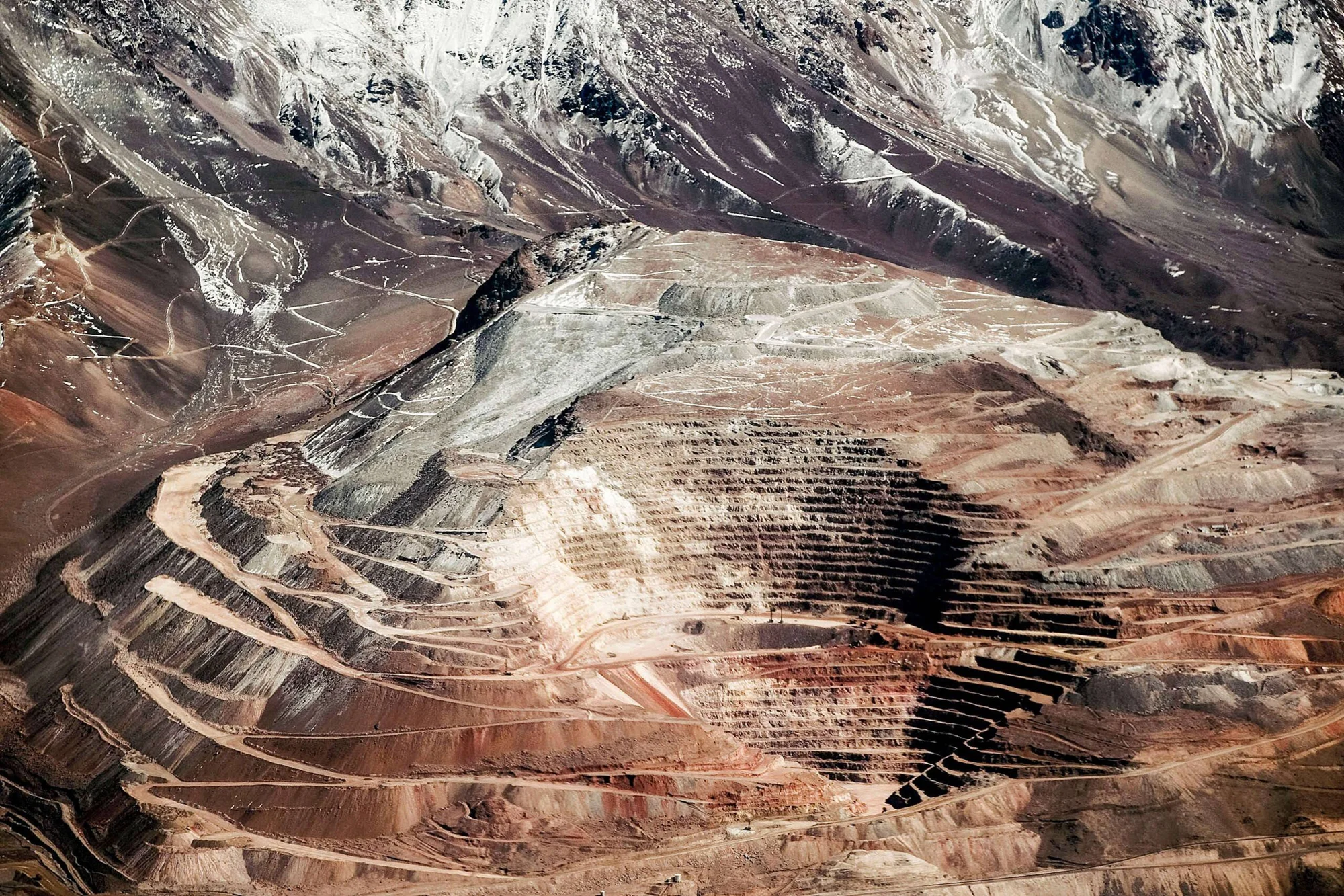 Mina a cielo abierto con terrazas escalonadas en la ladera de una montaña nevada, fotografiada desde el aire.