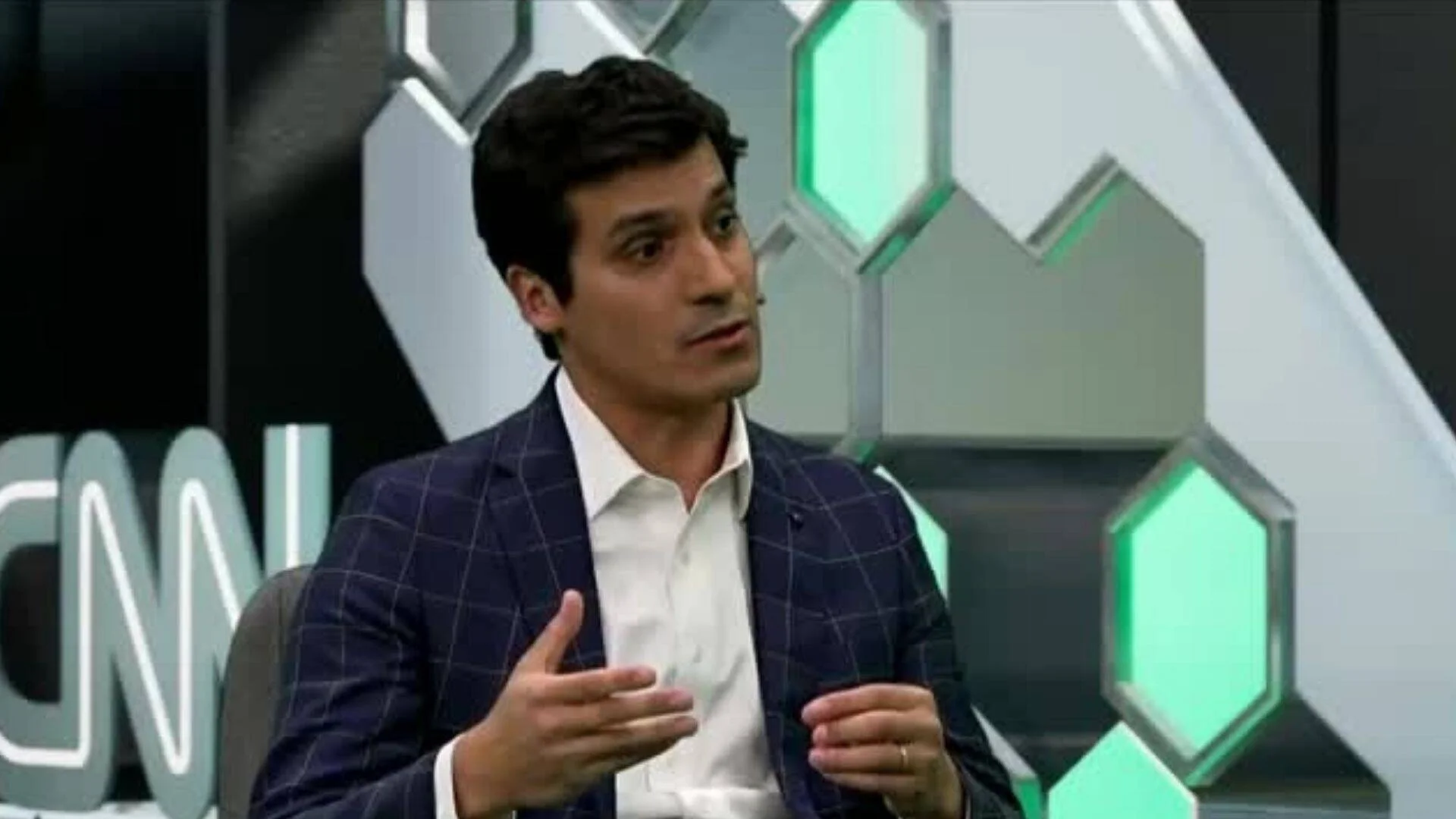 Hombre con saco a cuadros azul habla gesticulando con las manos en un estudio de televisión con logo de CNN visible.