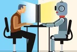 Un hombre y un robot sentados frente a frente en un escritorio compartido, cada uno usando una computadora.