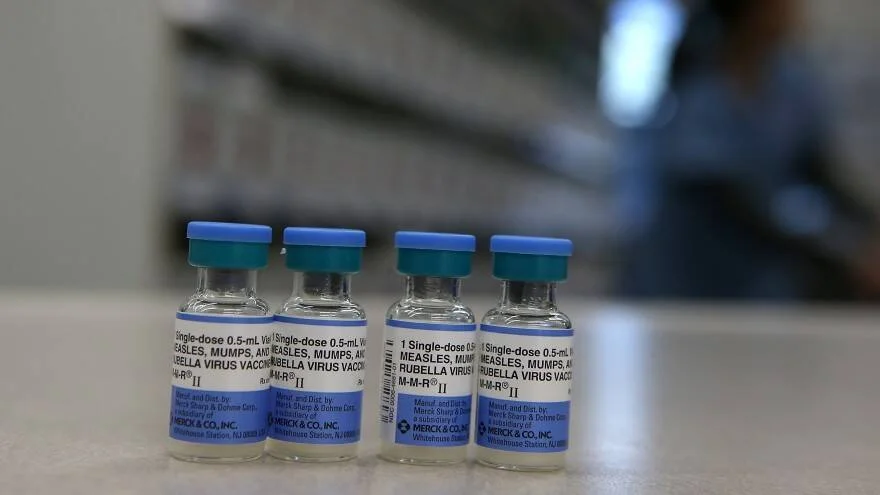 Cuatro viales de vacuna contra el sarampión, paperas y rubéola (MMR II) de Merck alineados sobre una superficie.