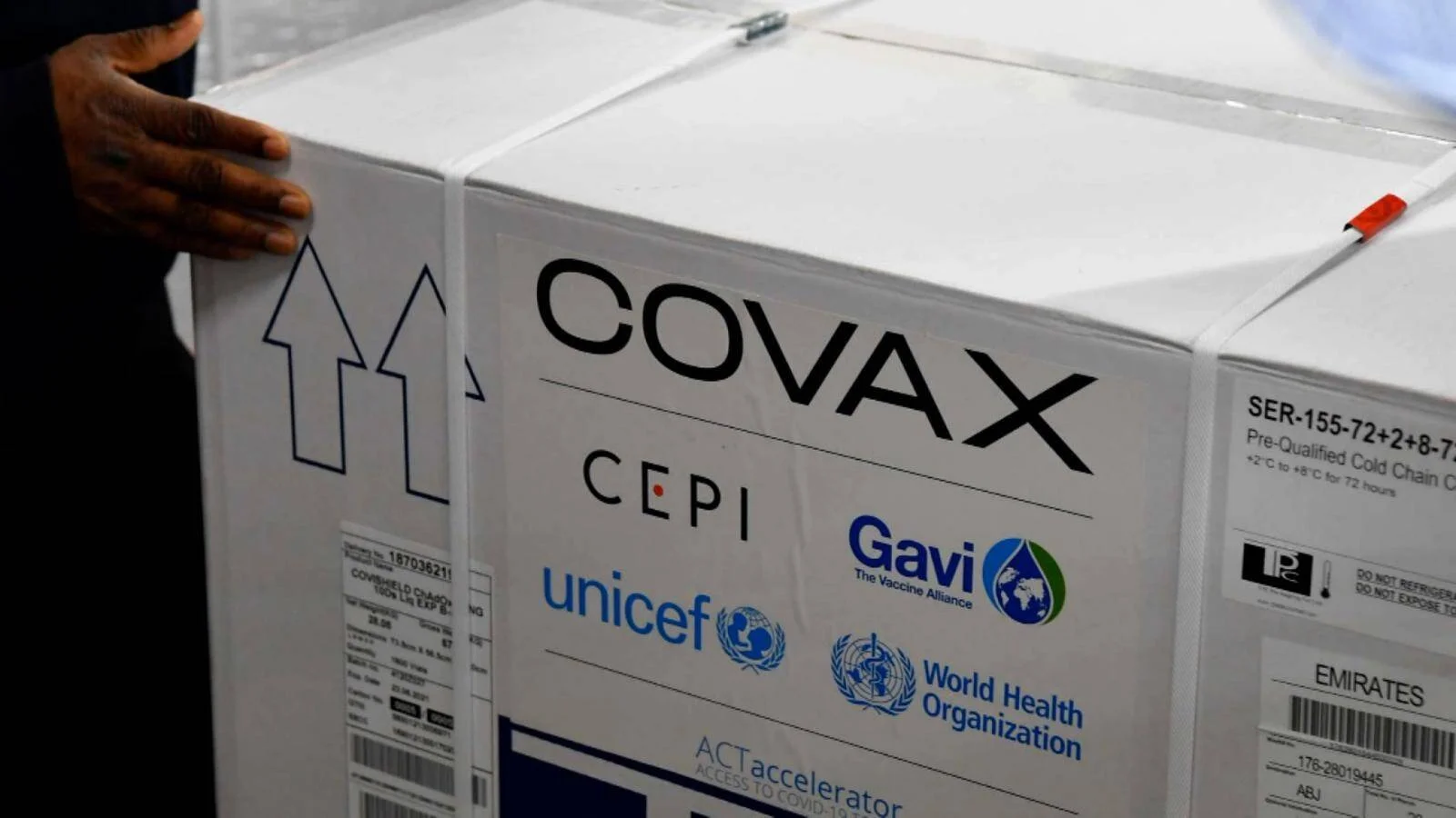 Una persona manipula una caja de vacunas del mecanismo COVAX con los logos de UNICEF, Gavi, OMS y CEPI.