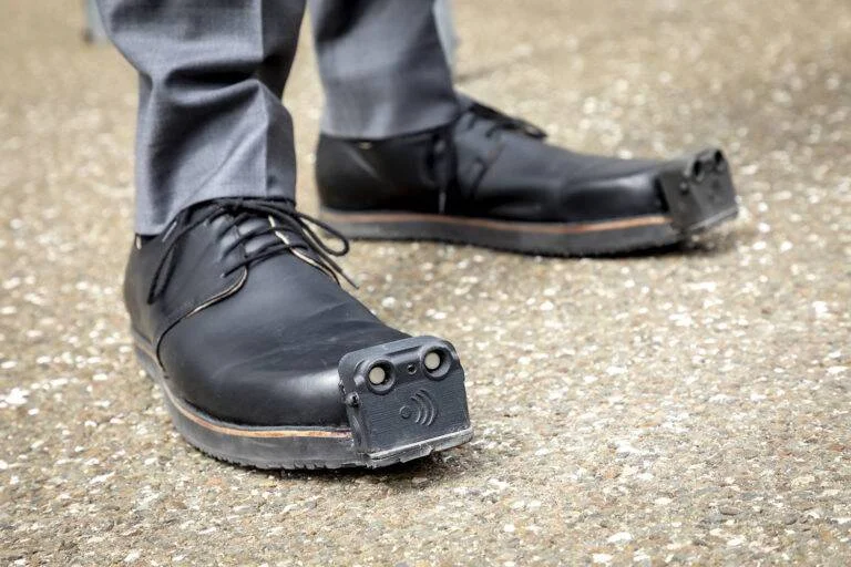 Pequeño dispositivo electrónico con sensores acoplado a la punta de un zapato negro de vestir.