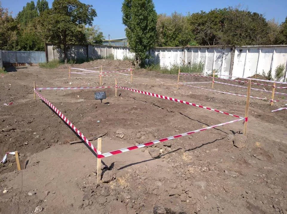 Terreno removido delimitado con cinta de señalización roja y blanca sobre estacas, con una placa identificadora en el interior.