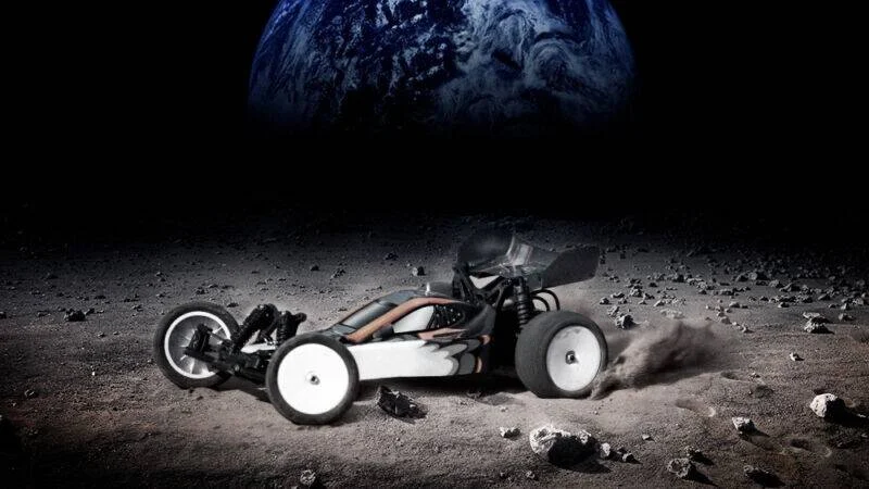 Buggy a radio control circula sobre suelo lunar rocoso con la Tierra visible en el cielo oscuro.