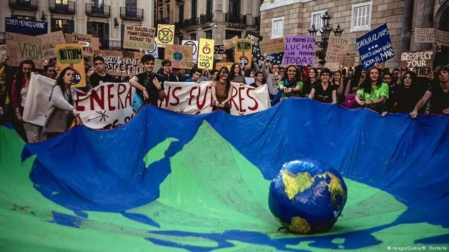 Jóvenes marchan por el clima sosteniendo una gran pancarta con un globo terráqueo y carteles en Barcelona.