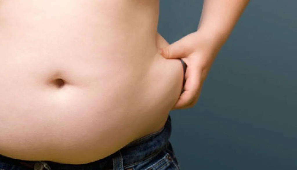 Niño pellizca el exceso de grasa en su abdomen, ilustrando el sobrepeso infantil.