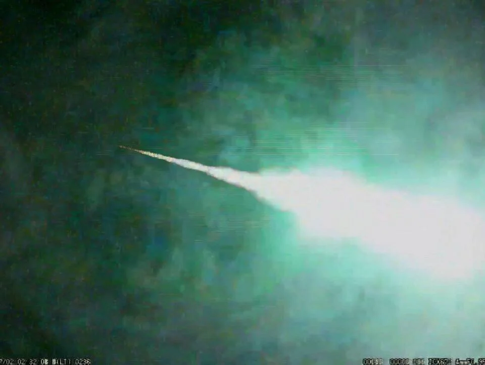 Bola de fuego con estela luminosa blanca cruzando el cielo nocturno, captada por cámara de vigilancia.