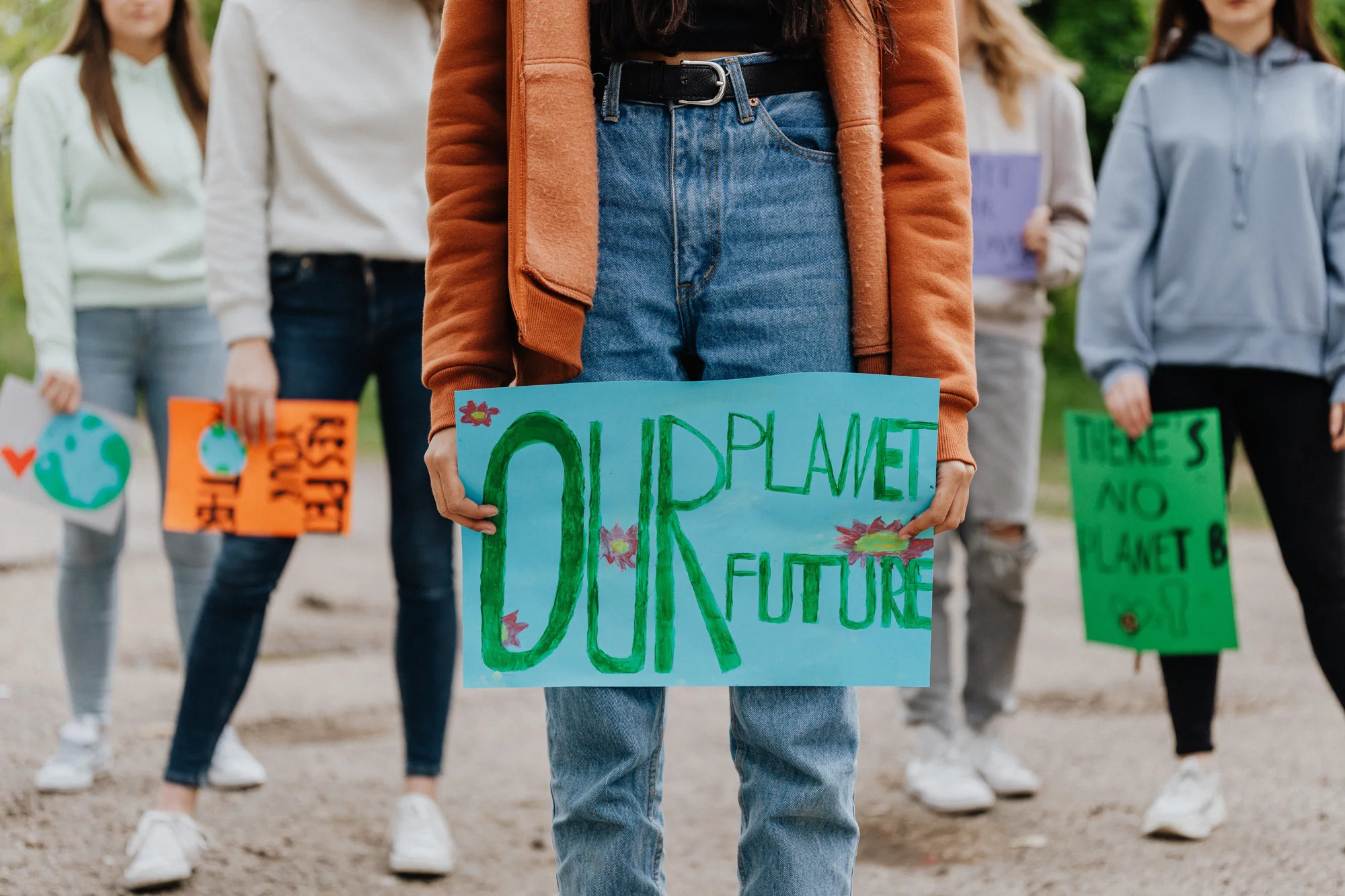 Grupo de jóvenes sosteniendo carteles en una protesta climática, con mensajes como 'Our Planet Our Future' y 'There's No Planet B'.