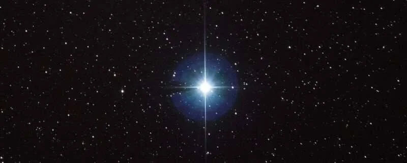 Estrella muy luminosa con destello en cruz y halo azulado, rodeada de estrellas distantes sobre fondo negro.