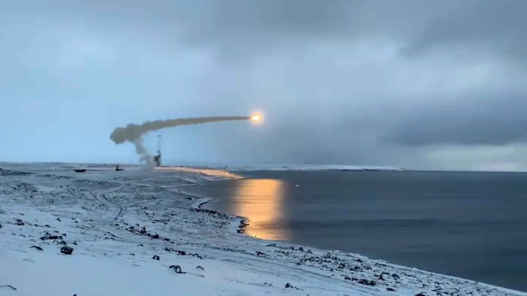 Un misil es lanzado desde una costa nevada y ártica dejando una estela de humo sobre el mar en un día nublado.