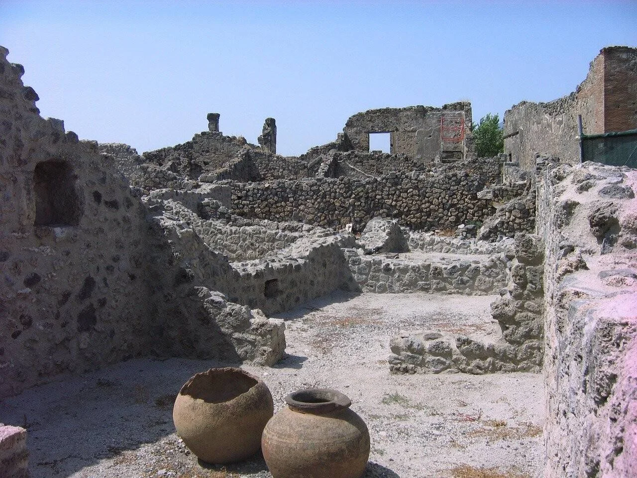 Ruinas de muros de piedra de una ciudad antigua con dos ánforas de cerámica en primer plano.