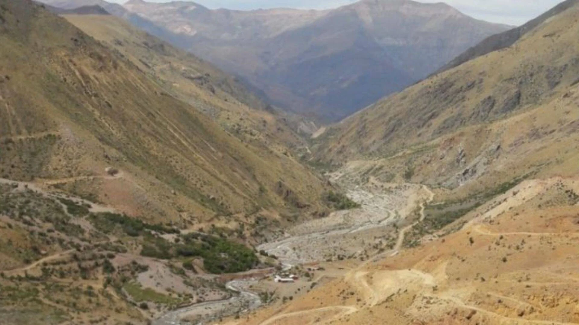 Vista aérea de un valle profundo entre montañas áridas con un cauce de río seco serpenteante y escasa vegetación.