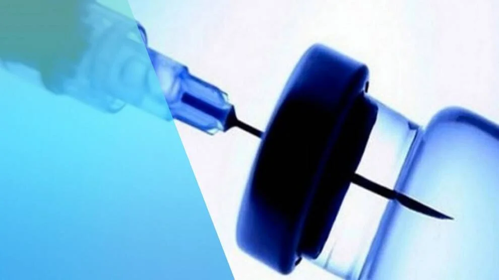 Aguja de jeringa atravesando el tapón de goma de un frasco de medicamento o vacuna, en tonos azules.