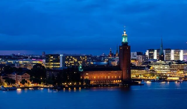 Vista nocturna del Ayuntamiento de Estocolmo con su torre iluminada reflejada sobre el agua durante la hora azul.