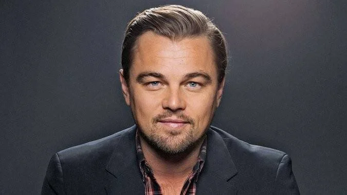 Hombre adulto de ojos claros, cabello castaño peinado hacia atrás y barba corta, vistiendo saco oscuro, posando ante fondo gris.
