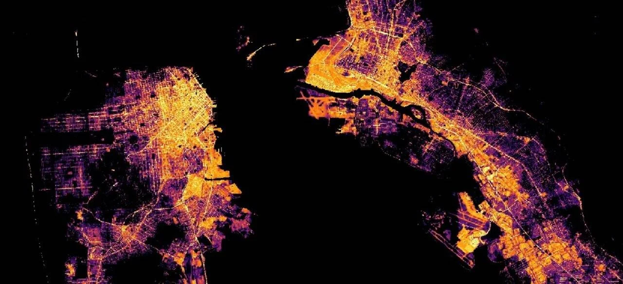 Vista satelital nocturna de dos zonas urbanas costeras separadas por agua, con calles y zonas densas iluminadas en naranja y púrpura.