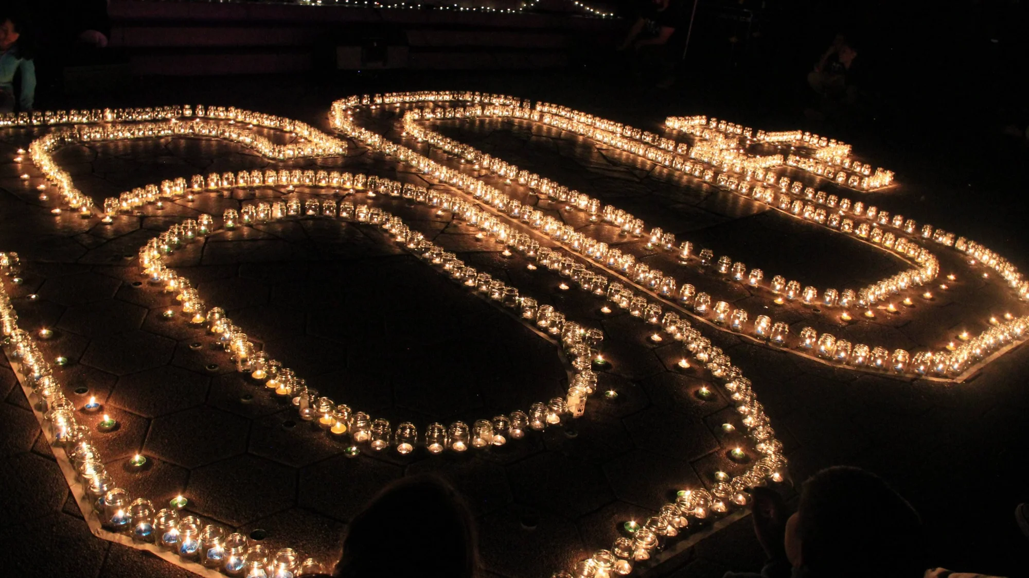 Cientos de velas en frascos de vidrio forman un laberinto iluminado sobre el pavimento en la oscuridad de la noche.
