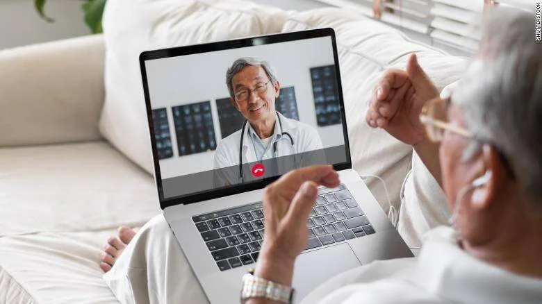 Persona mayor realiza una videollamada con un médico desde su hogar usando una laptop.