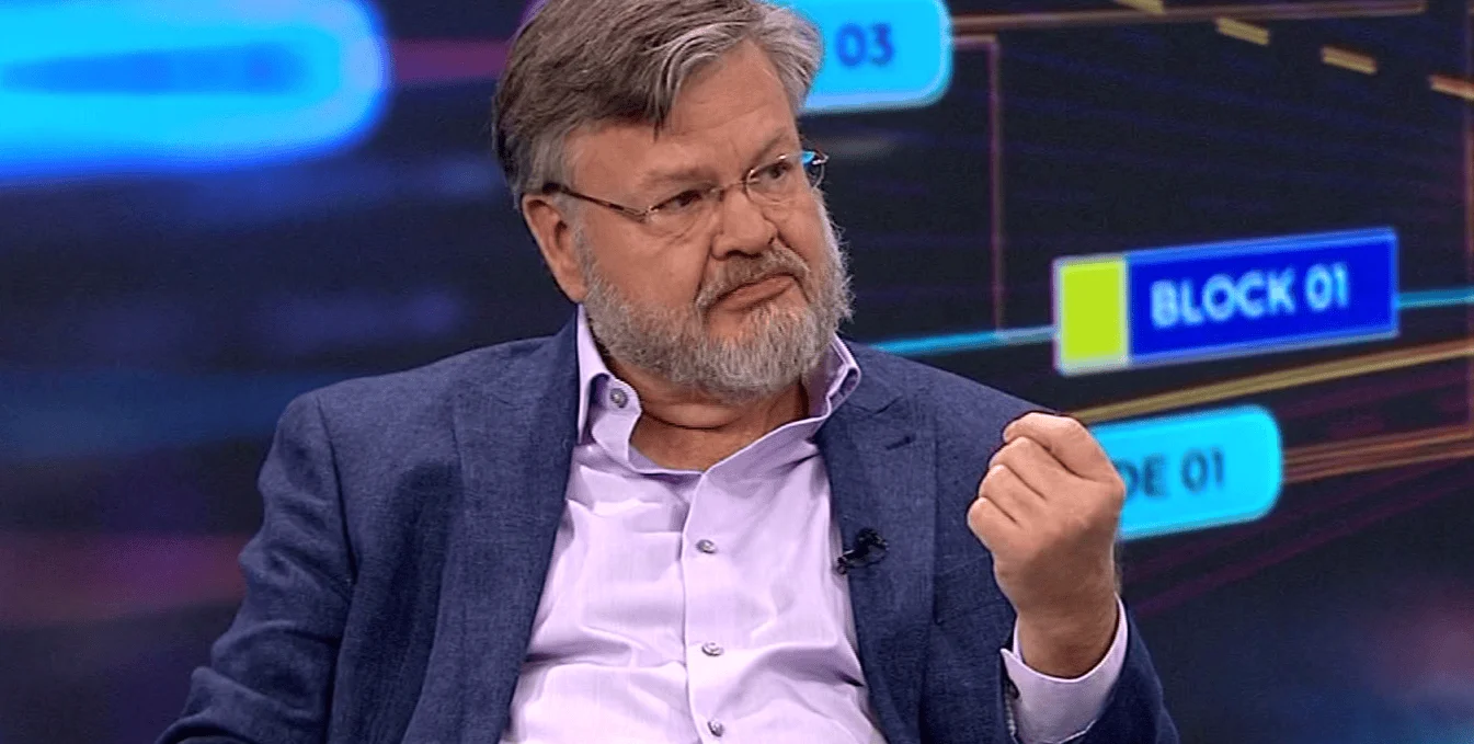 Hombre de mediana edad con anteojos y barba canosa gesticula con el puño durante una entrevista en un estudio de TV.