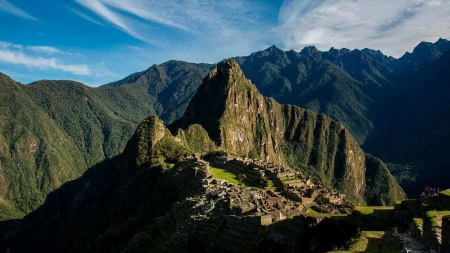 Vista panorámica de las ruinas de Machu Picchu rodeadas de montañas verdes y el pico Huayna Picchu al fondo.