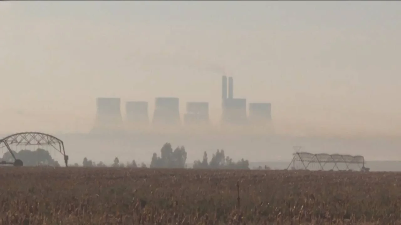 Torres de enfriamiento de una central eléctrica envueltas en smog, vistas desde un campo agrícola reseco en primer plano.