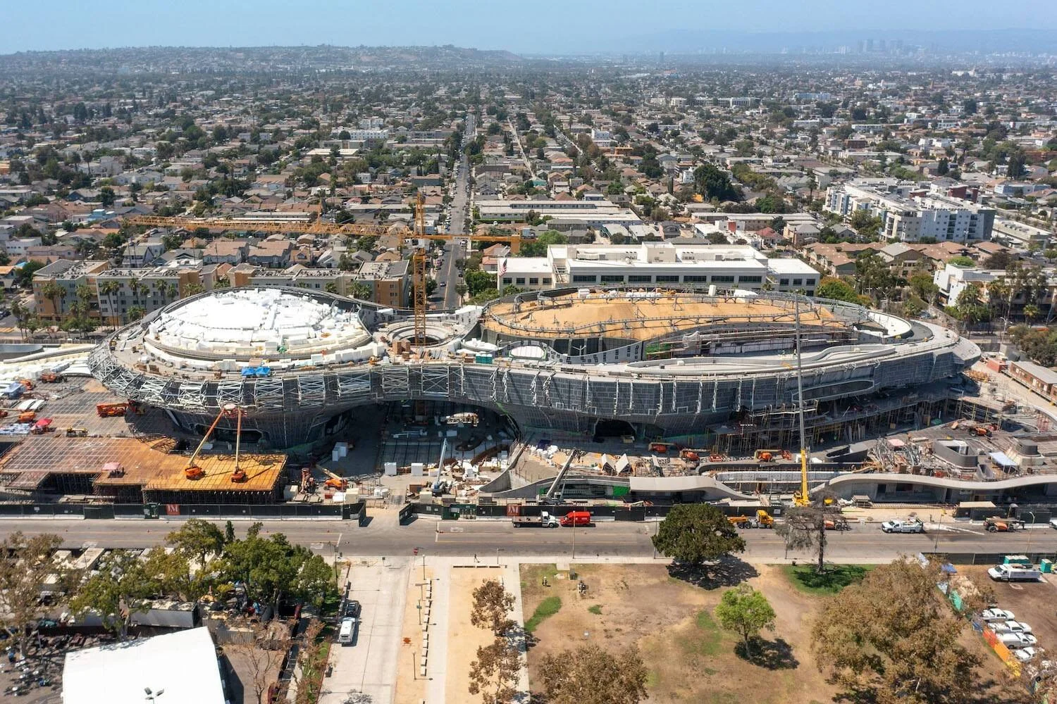 Vista aérea de un gran edificio de forma ovalada en construcción, rodeado de barrios residenciales de una ciudad estadounidense.