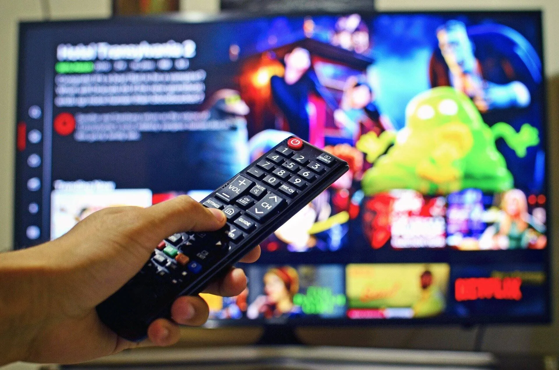 Mano sosteniendo un control remoto apuntando a un televisor con la interfaz de Netflix mostrando contenido animado.