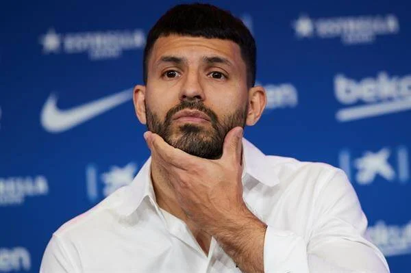 Hombre con camisa blanca apoya la mano en su mentón durante una conferencia de prensa ante fondo del FC Barcelona.