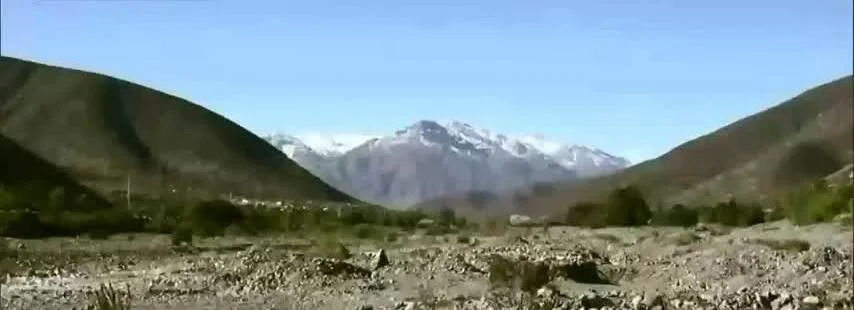 Valle árido entre cerros con montañas nevadas al fondo bajo un cielo azul despejado.