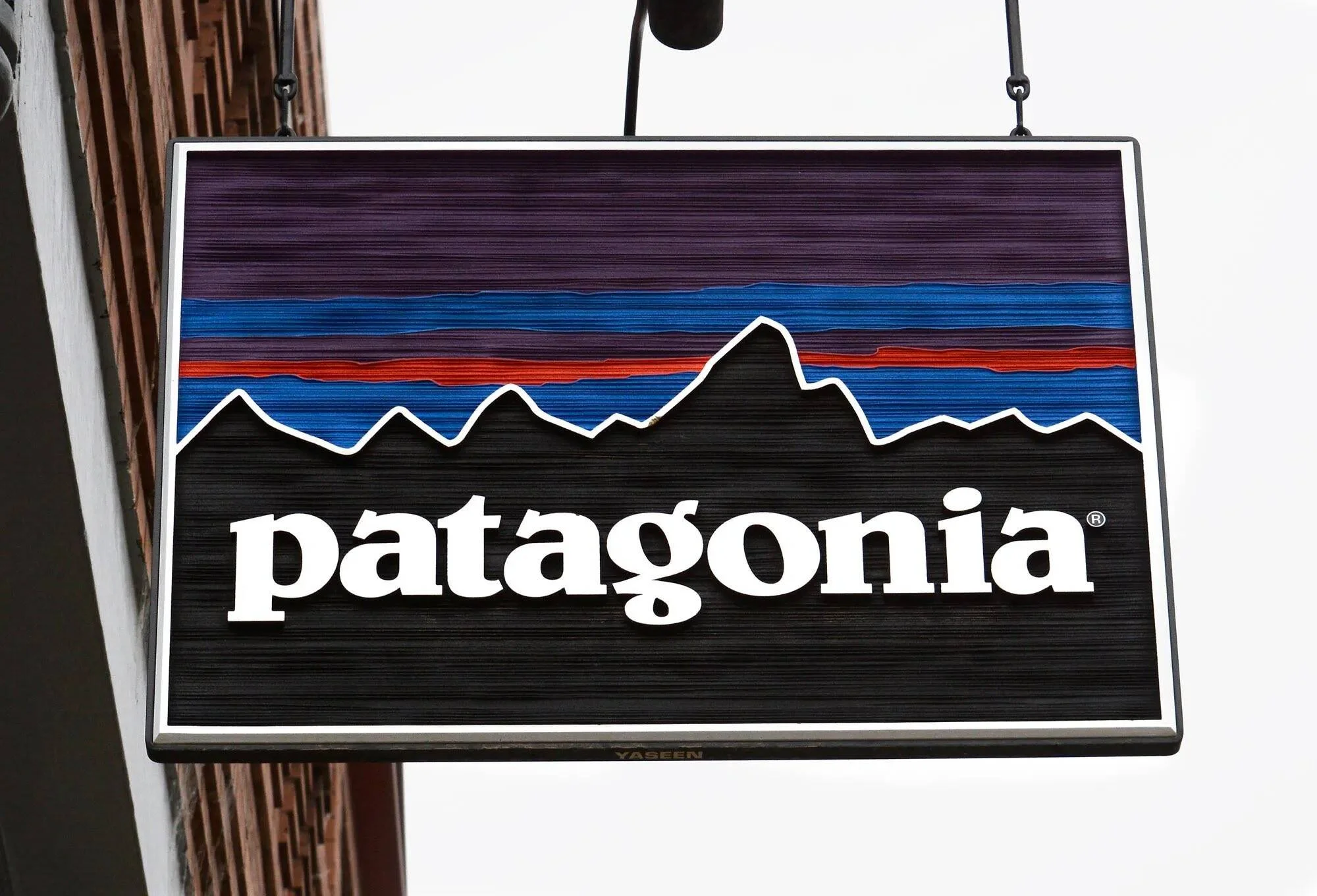 Letrero exterior de la marca Patagonia con su logo de montañas y cielo colorido, colgado frente a una tienda.