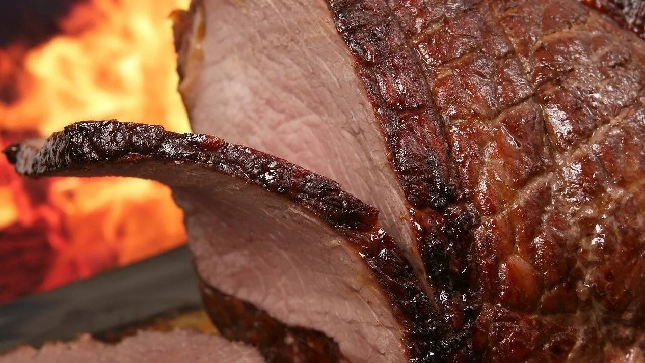 Corte de carne asada con costra caramelizada al exterior y carne rosada al interior, con llamas al fondo.
