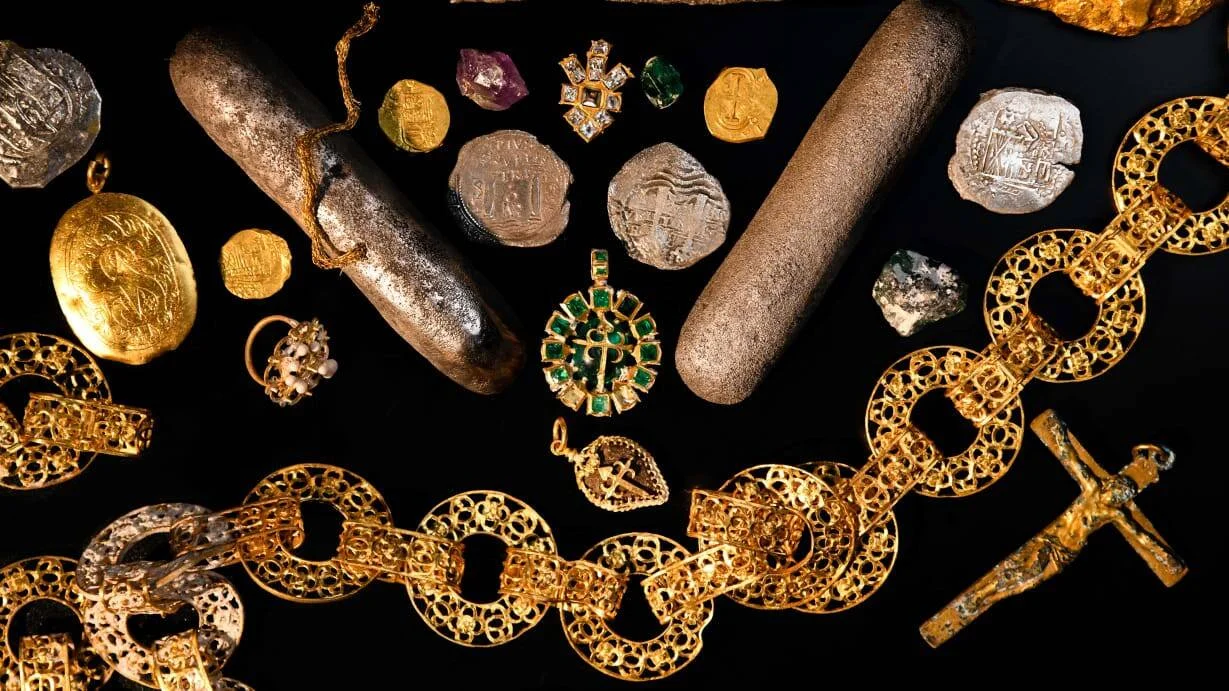 Colección de artefactos recuperados de naufragio: monedas de oro y plata, lingotes, cadenas doradas, pendientes con esmeraldas y una cruz.