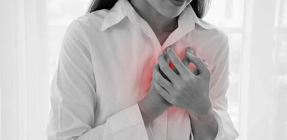 Mujer sostiene su pecho con ambas manos; la zona del corazón aparece resaltada en rojo, indicando dolor o malestar cardíaco.