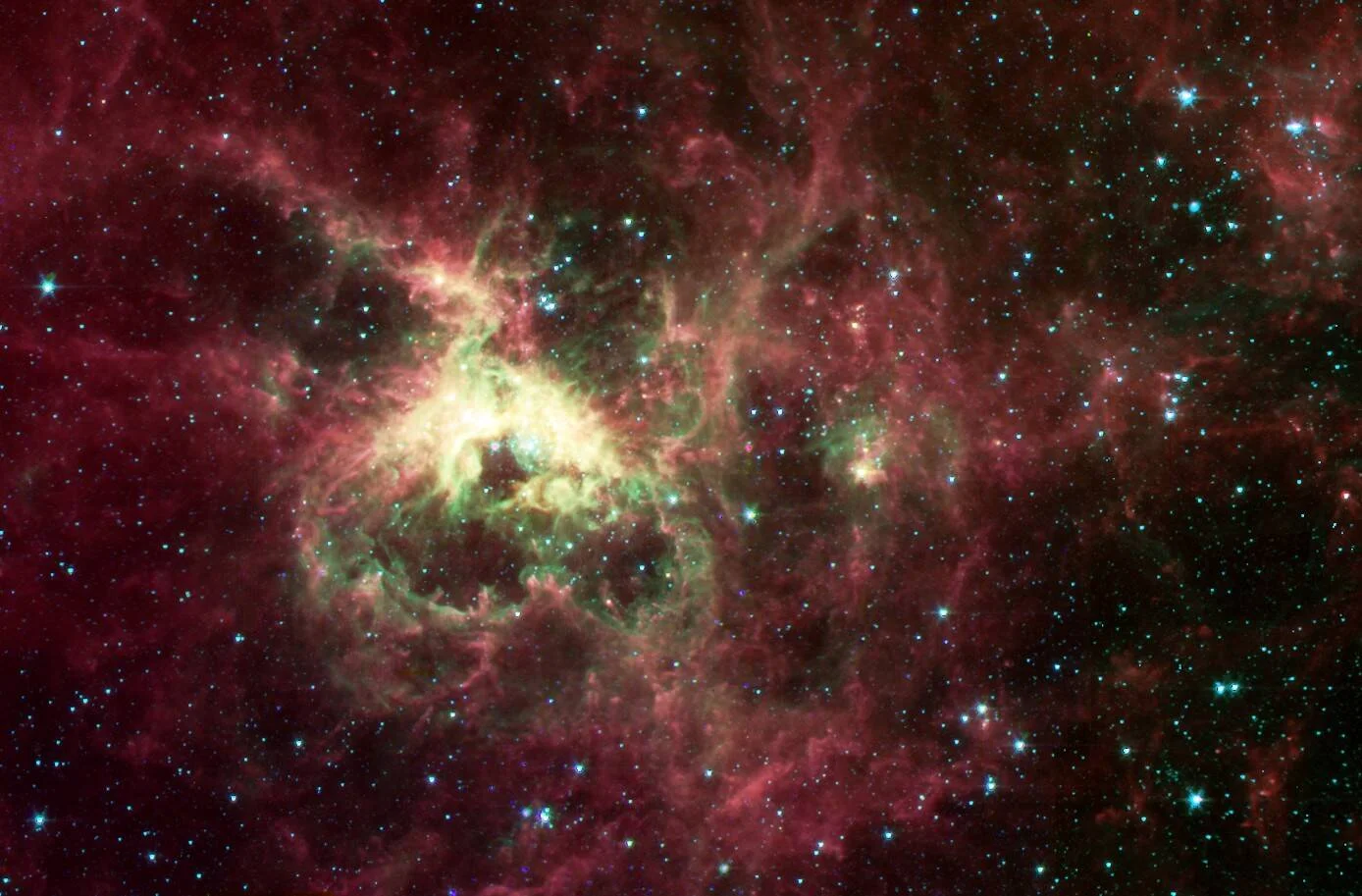 Nebulosa cósmica con nubes de gas en rojo y verde rodeadas de miles de estrellas azules, captada en infrarrojo.