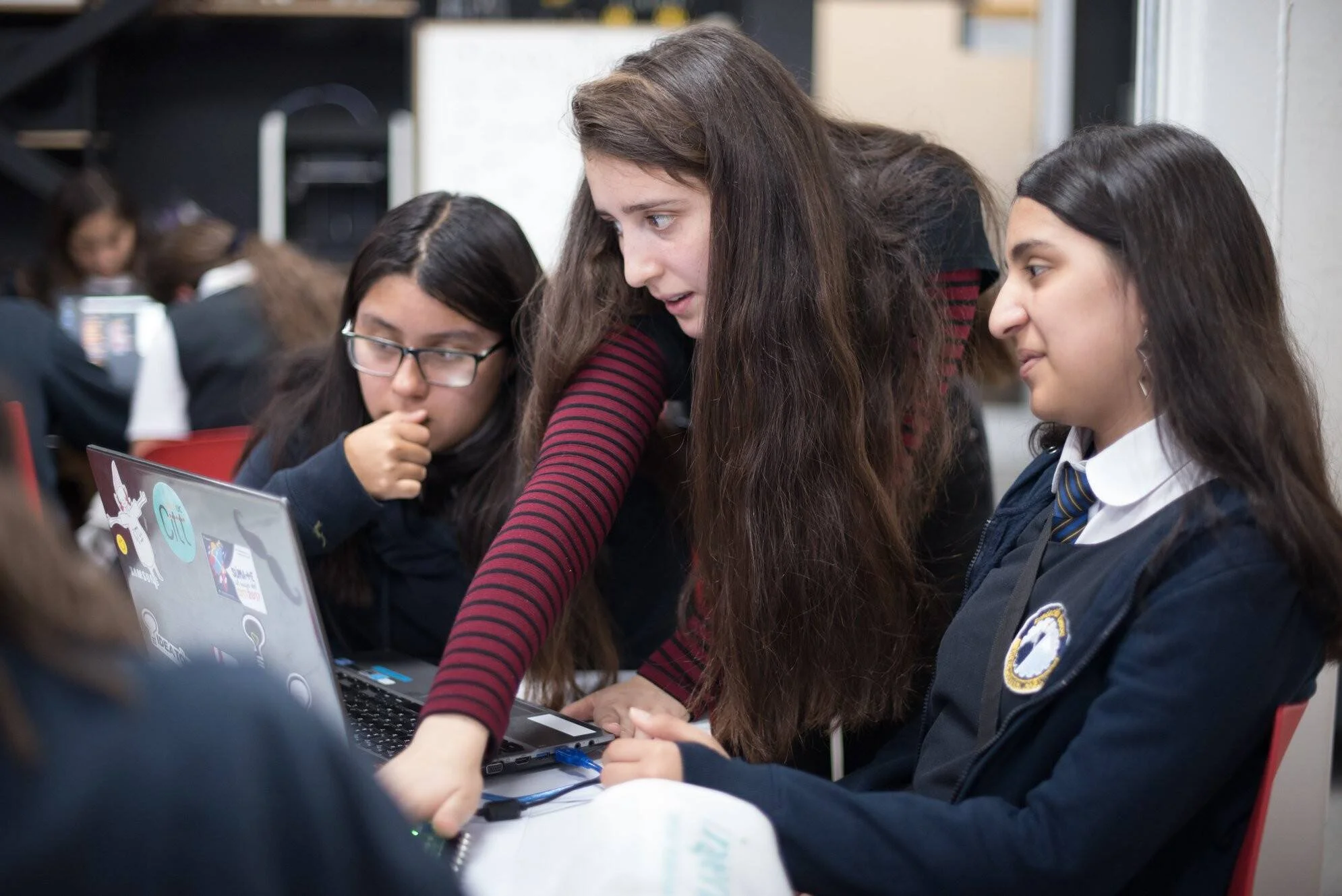 Tres estudiantes con uniforme escolar colaboran frente a una laptop durante una actividad en el aula.