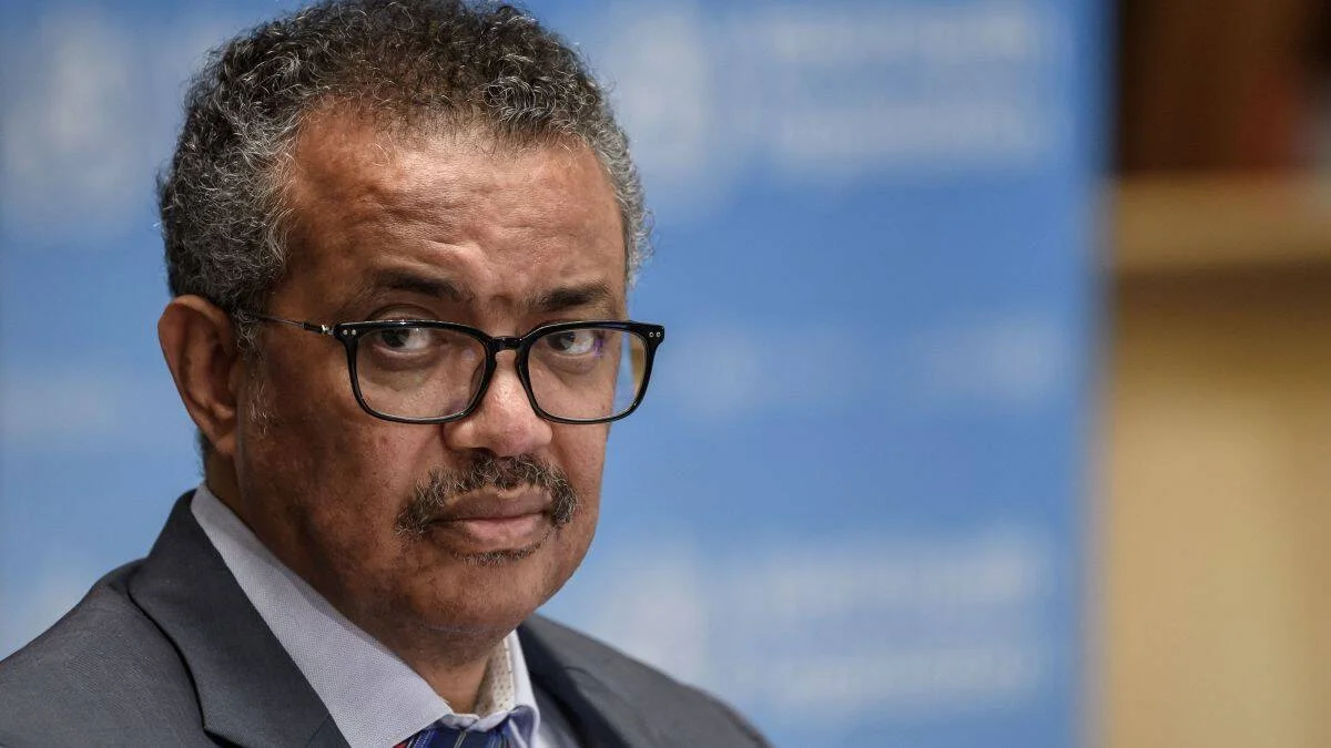 Hombre con lentes de armazón negra y traje gris con expresión seria ante un fondo azul con logo institucional.