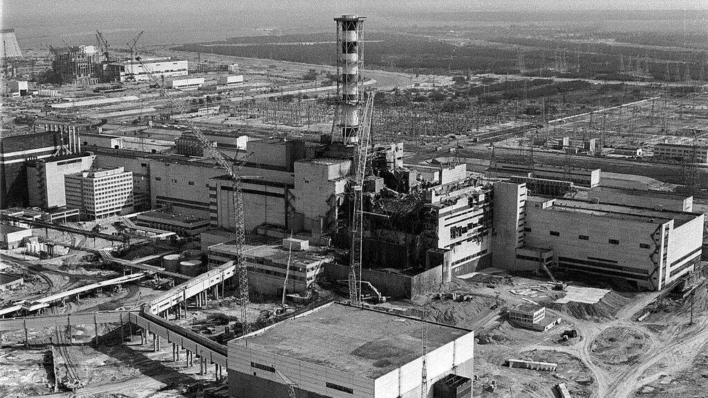 Vista aérea en blanco y negro de la central nuclear de Chernóbil con el reactor 4 destruido y grúas de construcción alrededor.