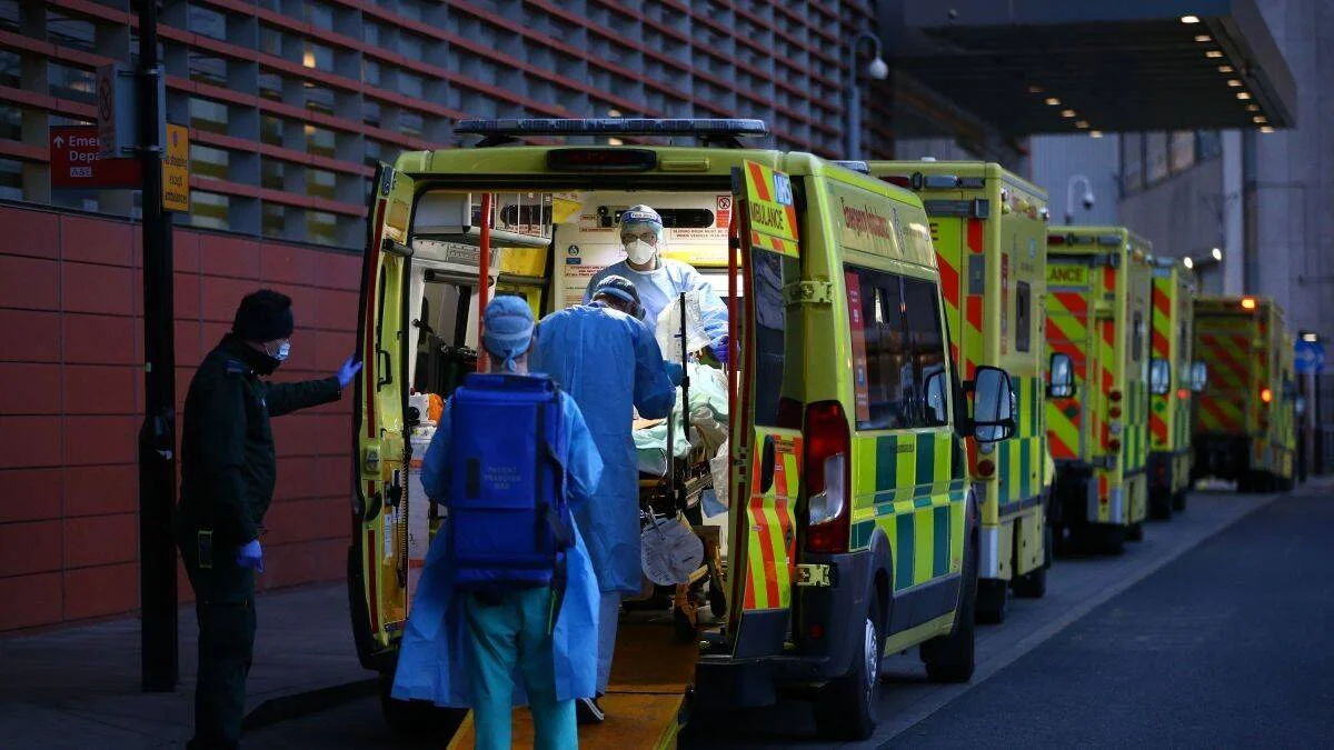 Personal sanitario con equipo de protección descarga a un paciente de una ambulancia del NHS frente a urgencias hospitalarias.