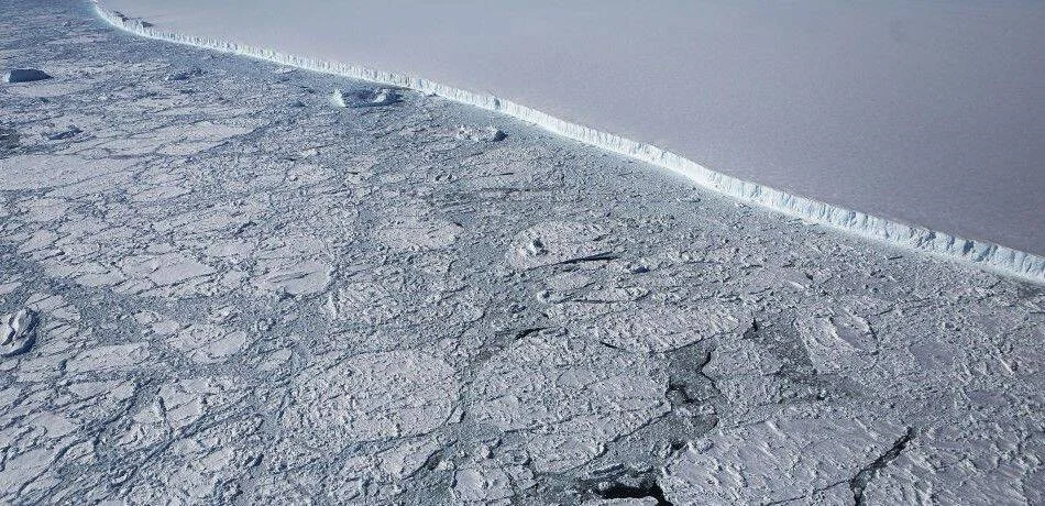 Vista aérea de un enorme iceberg tabular junto a hielo marino fragmentado en la Antártida.