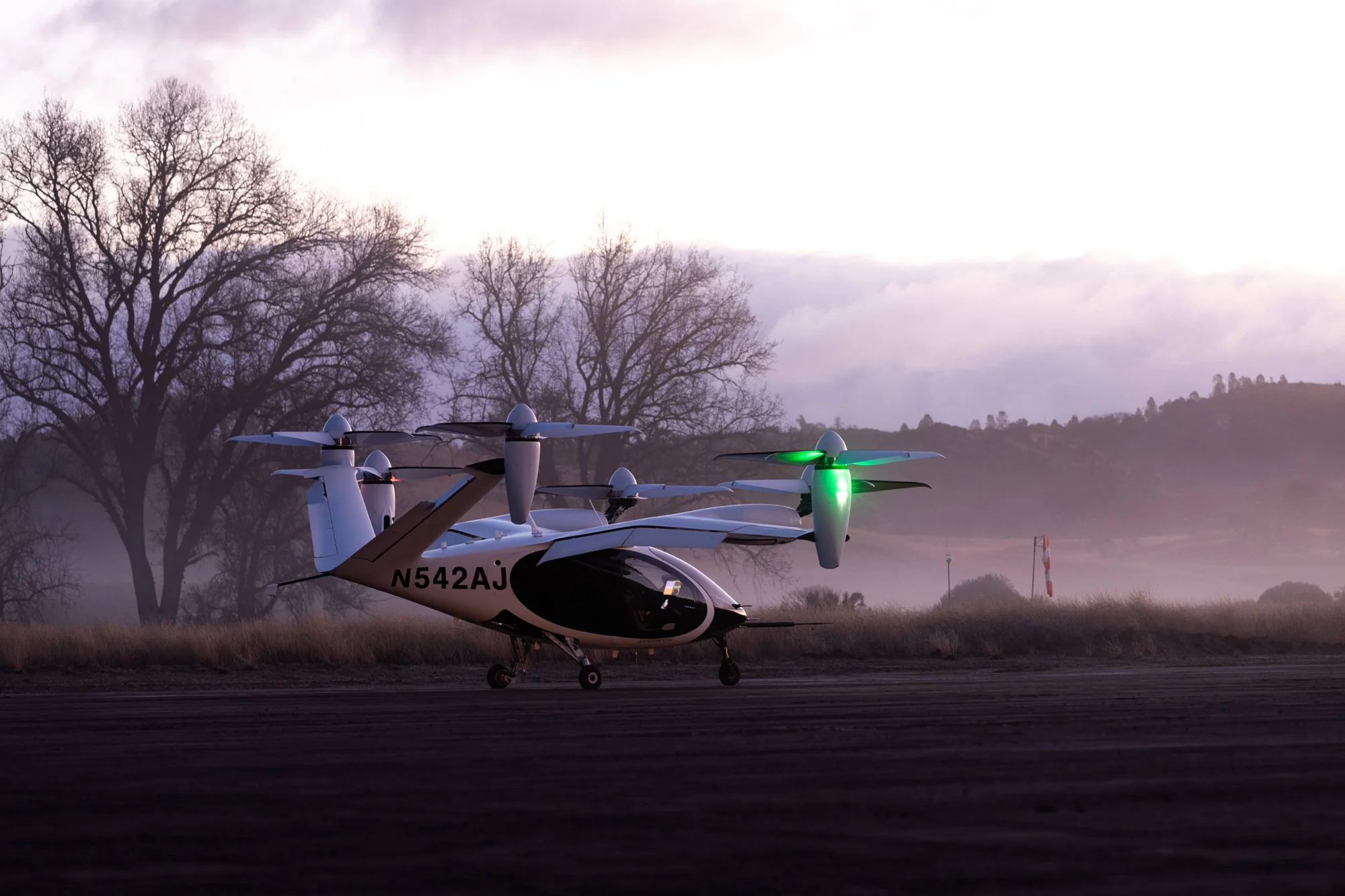 Aeronave eléctrica de despegue vertical (eVTOL) con matrícula N542AJ en una pista al amanecer, con rotores iluminados en verde.