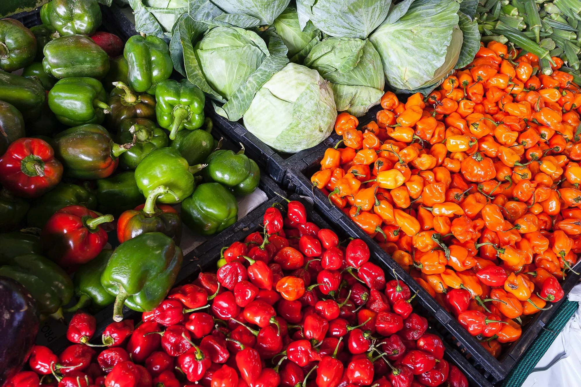Cajones con pimientos verdes, rojos y naranjas, repollos y otros vegetales frescos en un puesto de mercado.