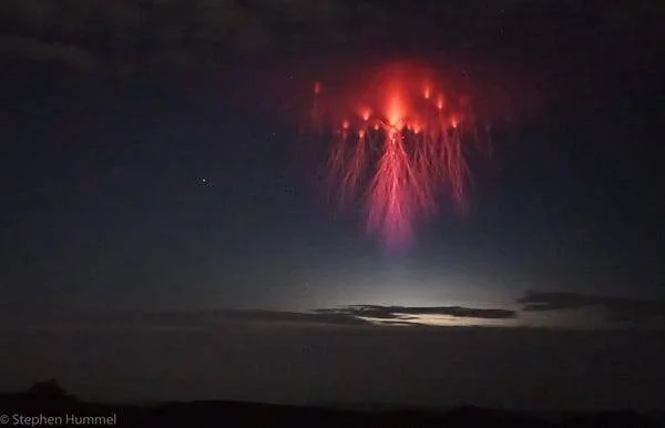 Múltiples duendes rojos, fenómenos luminosos transitorios de color rojo y rosa, se elevan sobre nubes de tormenta en el cielo nocturno.